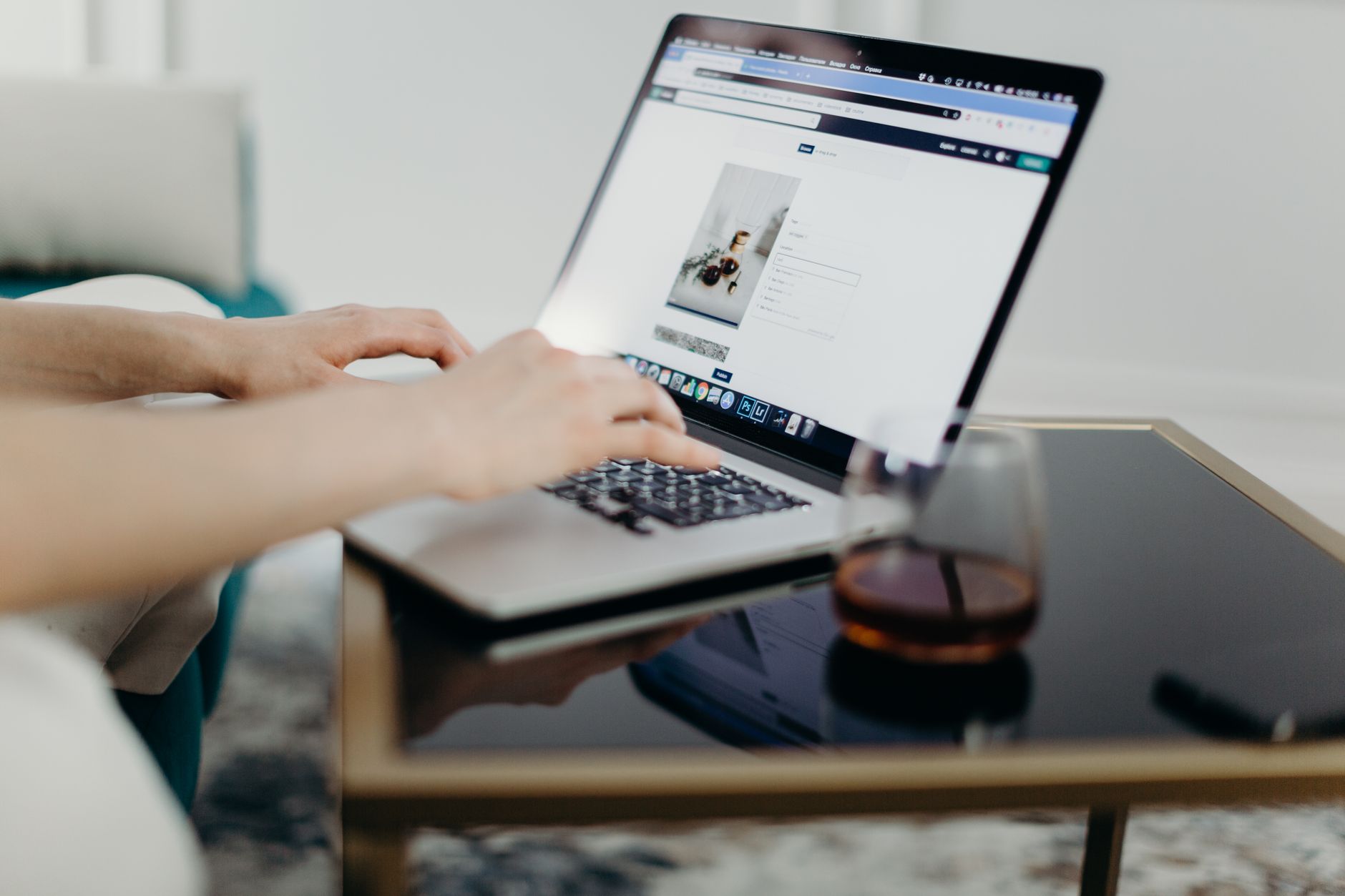 Persona che digita su un laptop in un home office curato, con un bicchiere vicino.