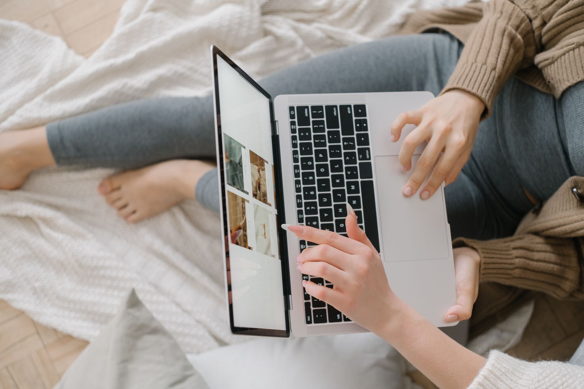 Donna appoggiata al letto che usa un laptop, sfogliando immagini.
